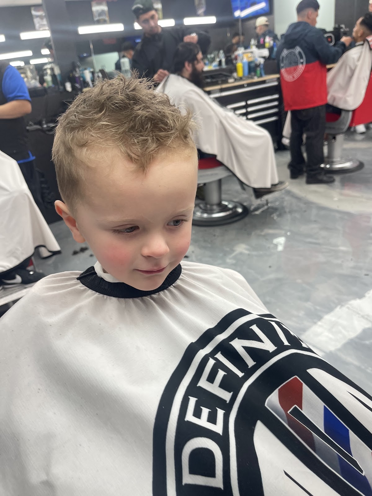 Kid fresh cut in Definite cape with busy shop behind